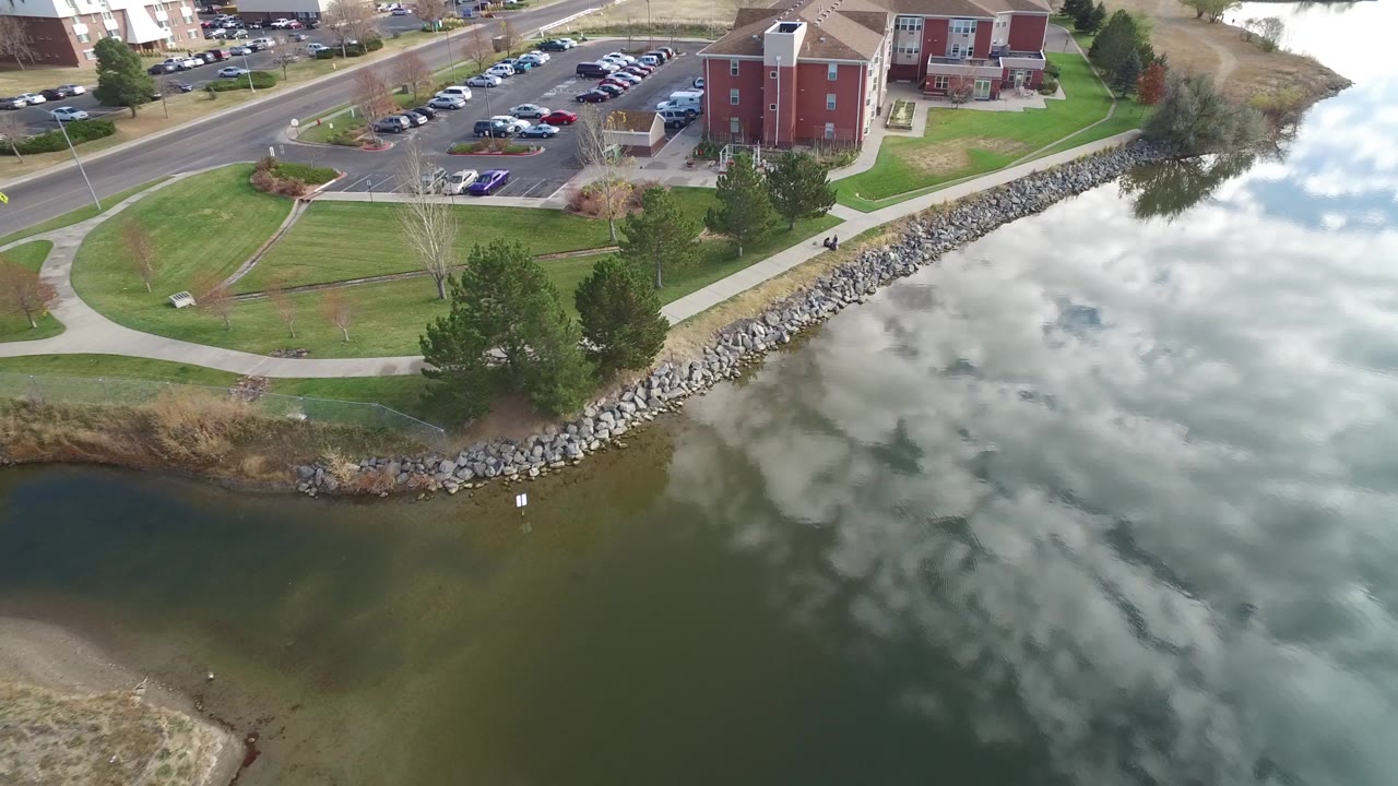 Aerial view of lake water, rock shoreline, lawns, parking lot, and red-brick residential buildings.