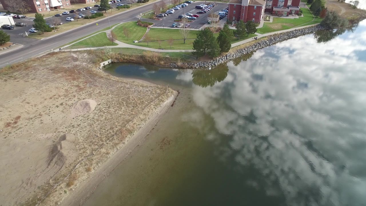 Aerial view of a dirt lot beside reflective lake water and a road.