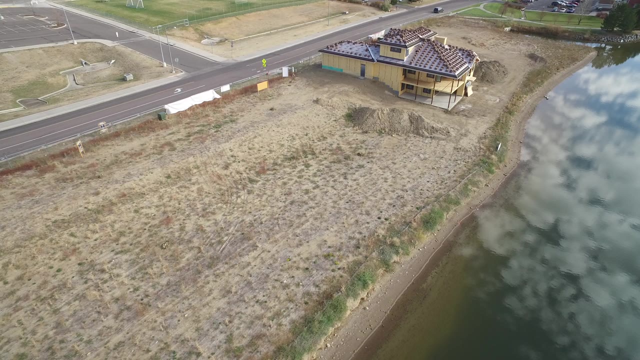 Aerial frame in Hidden Lake, Colorado showing dry open land beside green lake water, a roadside house near the top edge, and no visible people.
