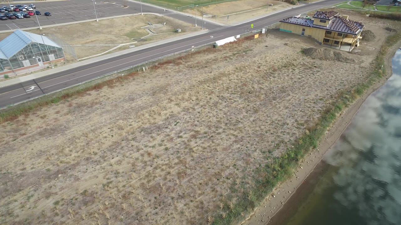 Aerial view of a graded dirt lot beside a road and water channel.