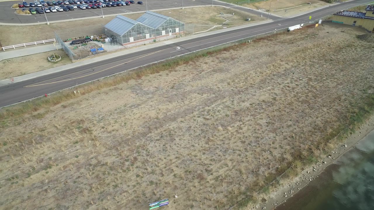 Aerial view of dry open land near a road with parked cars in the background.