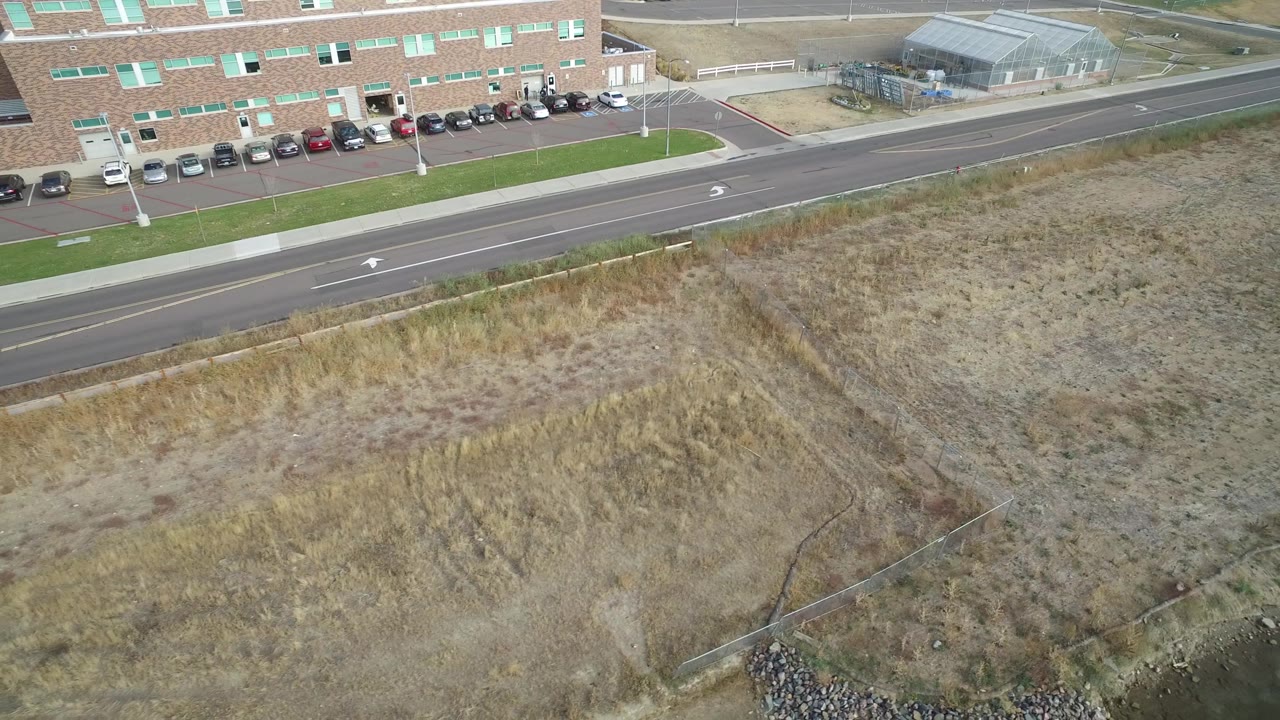 Aerial view in Hidden Lake, Colorado with the road running across the upper frame, a row of parked cars by the brick building, and scrubby ground filling the foreground with no visible people.
