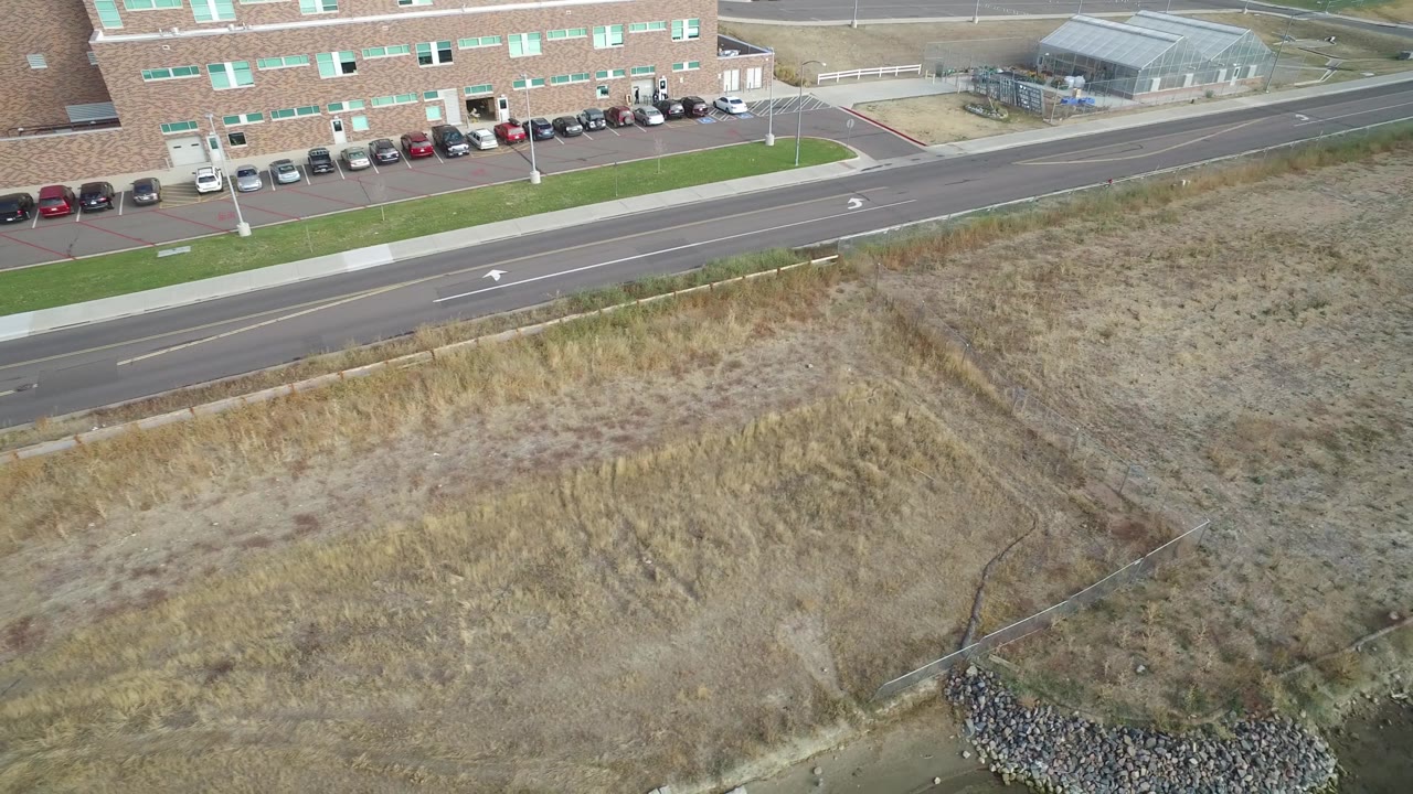 Aerial roadside view with building, parked cars, dry field, and waterline.