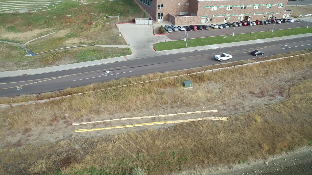 Aerial view of a road, dry grass, and a brick building with parked cars.