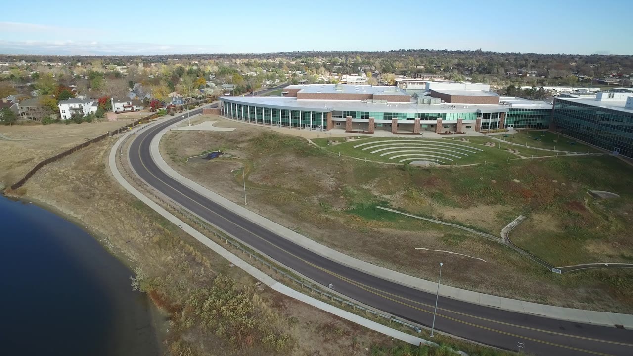 Wide aerial composition of road, lake edge, amphitheater-like lawn pattern, and building.