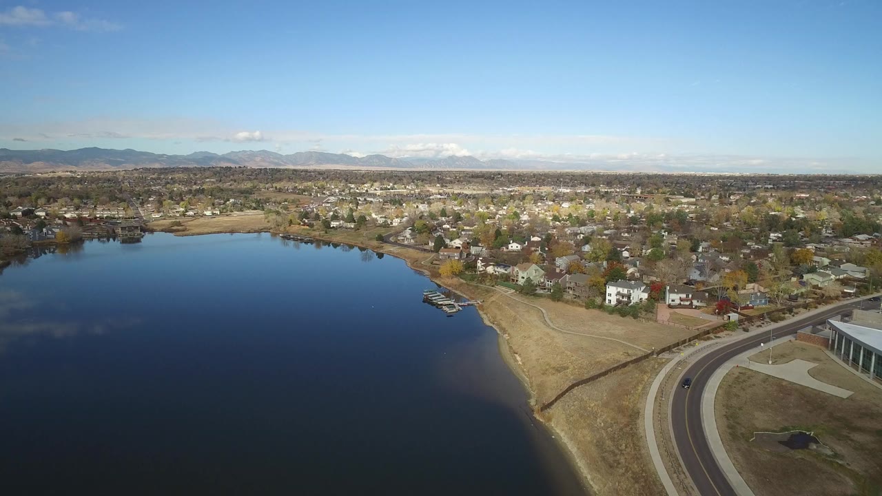 Aerial view of a lake beside houses, a road, and distant mountains.