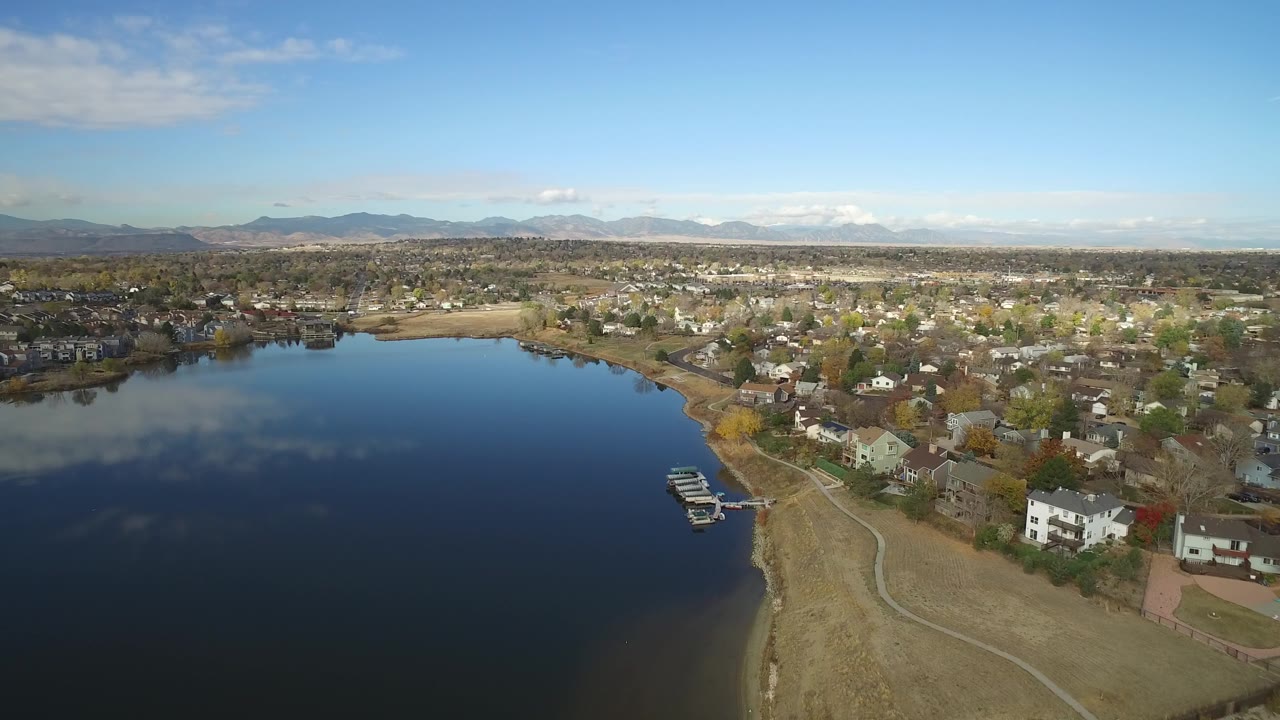 Aerial view of a blue lake beside homes and distant mountains.