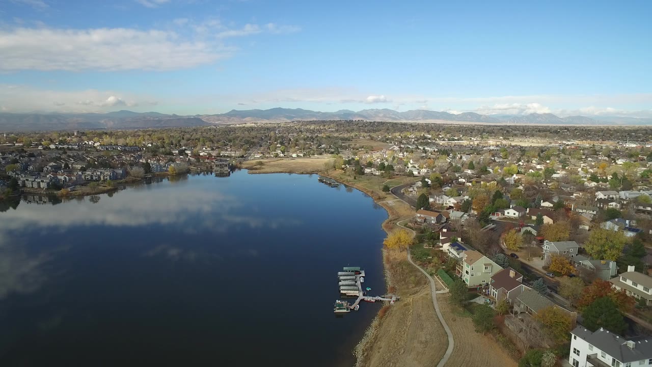 Aerial view of a dark lake beside homes and distant mountains.