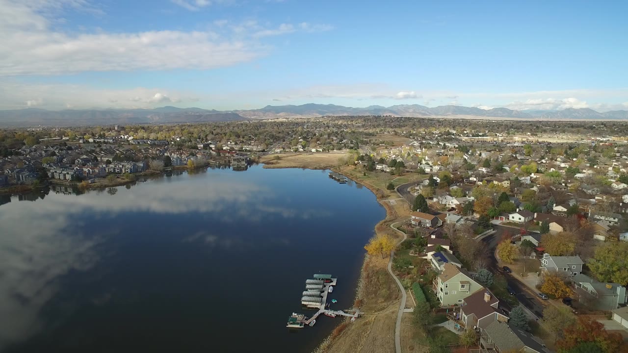 Aerial view of a lake beside residential houses and distant mountains.