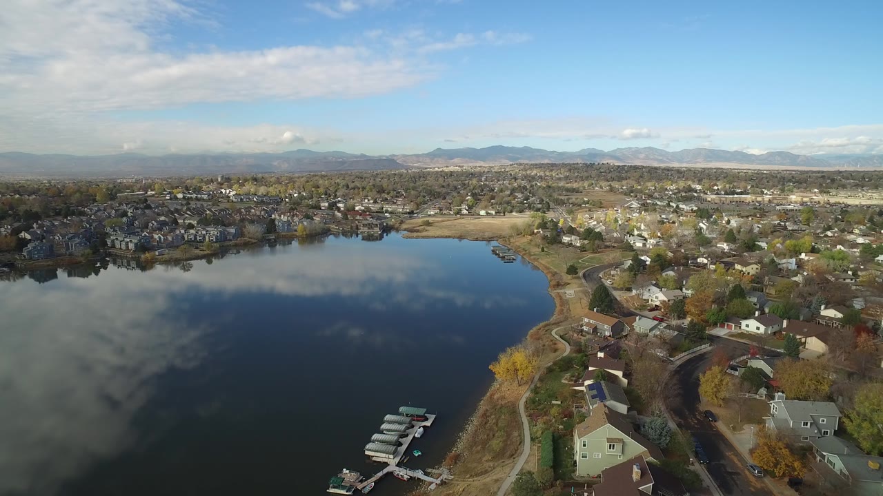 Aerial view over a lake, docks, homes, and distant mountains.