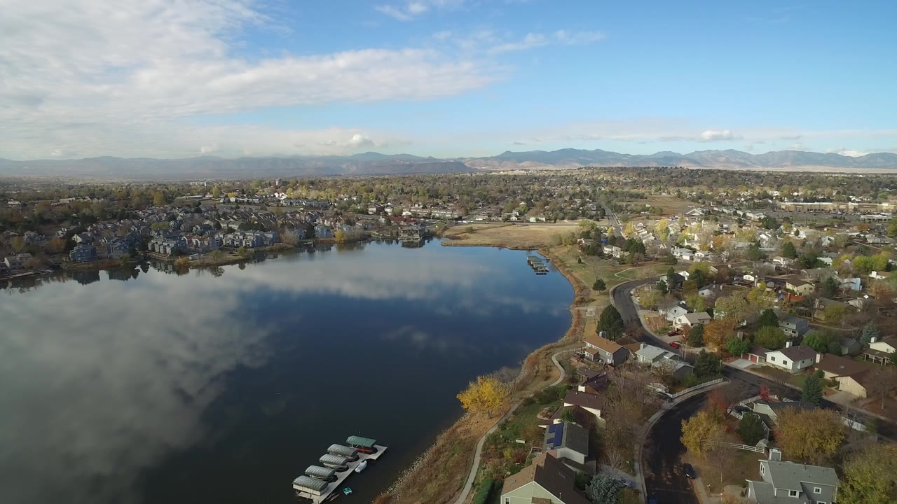 Aerial view of a lake beside a residential neighborhood and distant mountains.