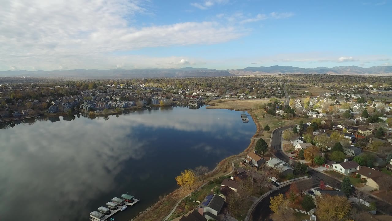Aerial view over Hidden Lake, Colorado, showing cloud reflections on dark water, small docks near the lower edge, neighborhood houses to the right, and no visible people.