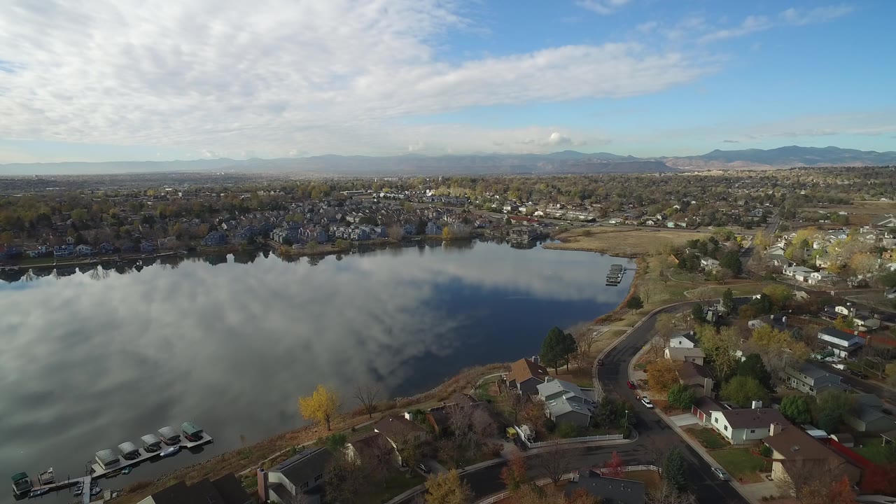 Aerial view over Hidden Lake, Colorado, showing cloud reflections across the water, clustered homes beyond the far shore, small docks near the lower edge, and no visible people.