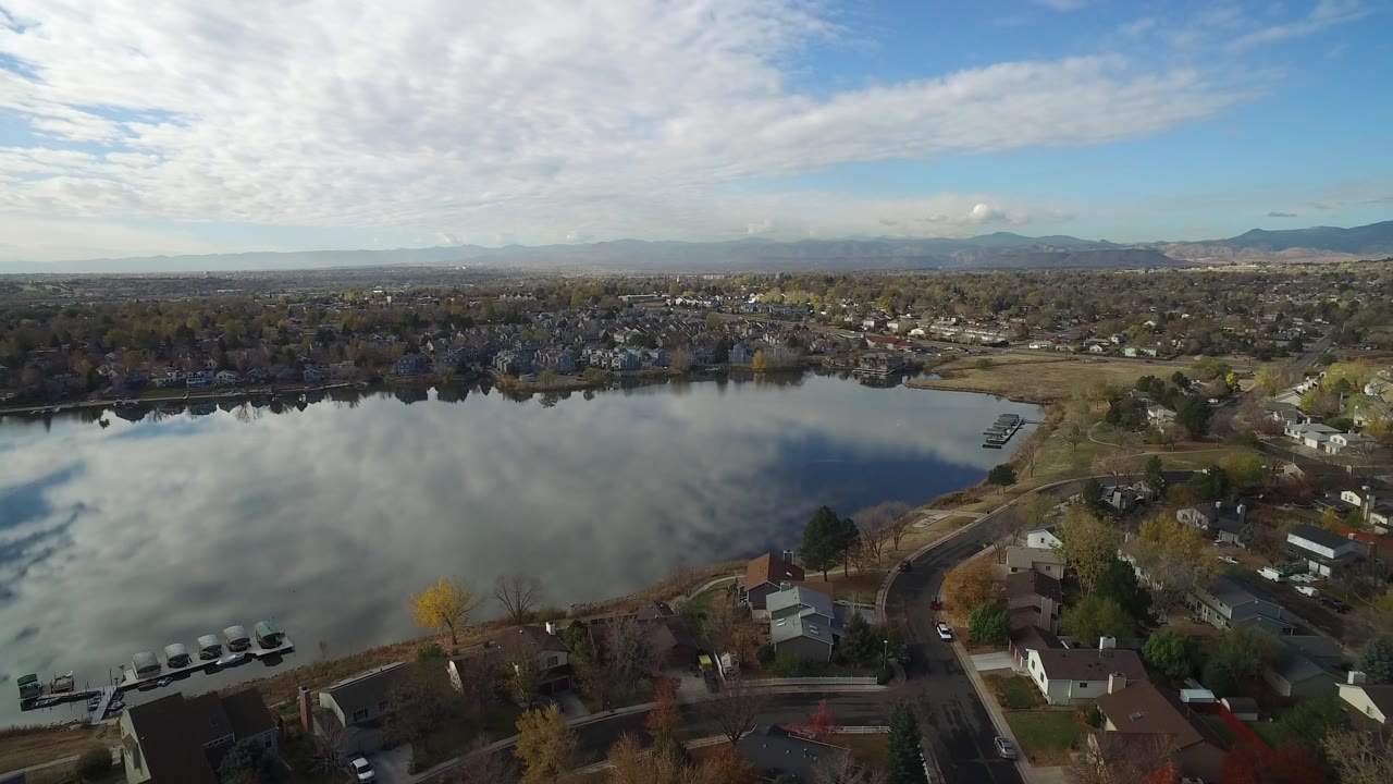 Aerial view over a reflective pond beside suburban homes and trees.