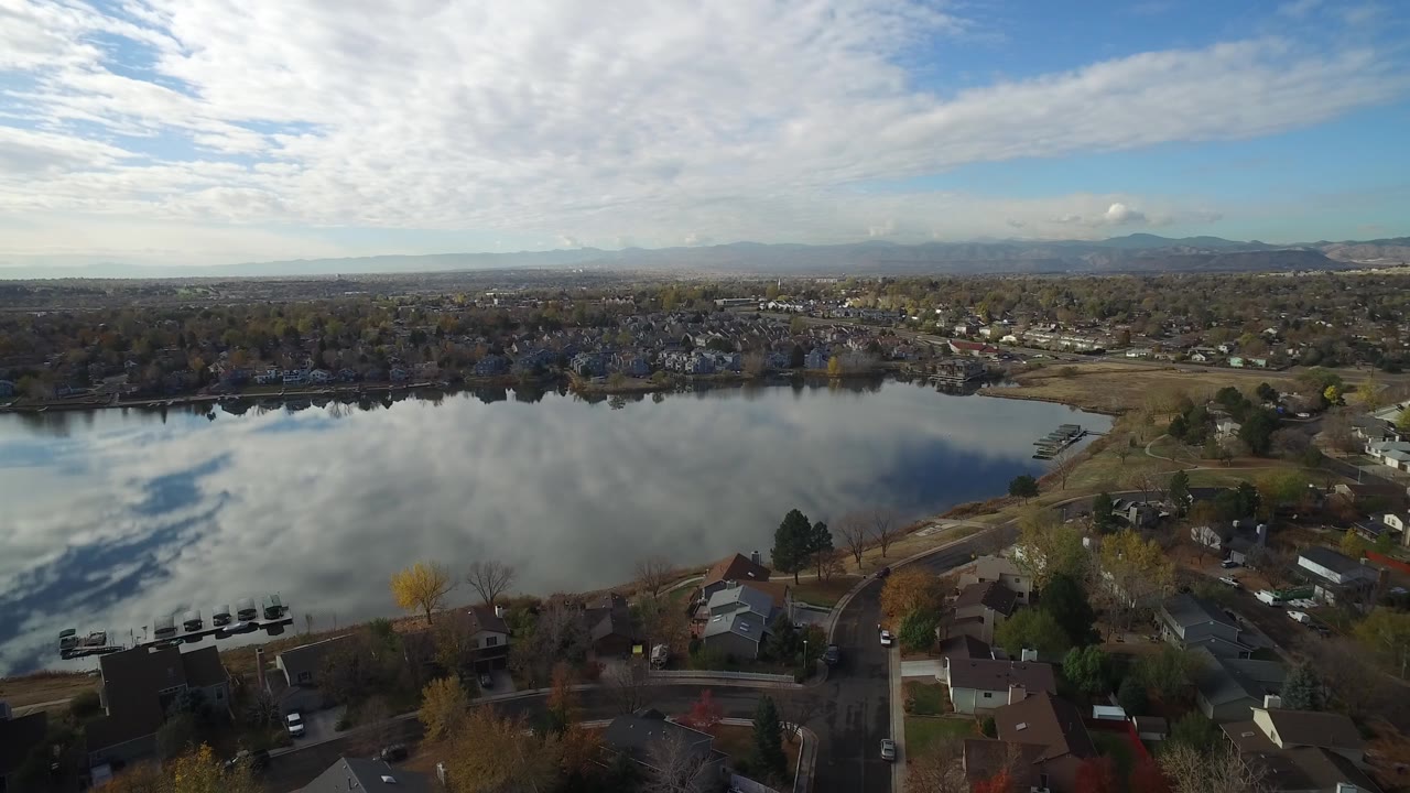 High aerial frame of Hidden Lake, Colorado with smooth water reflections, residential blocks along the shore, distant mountain ridges, and no visible people.