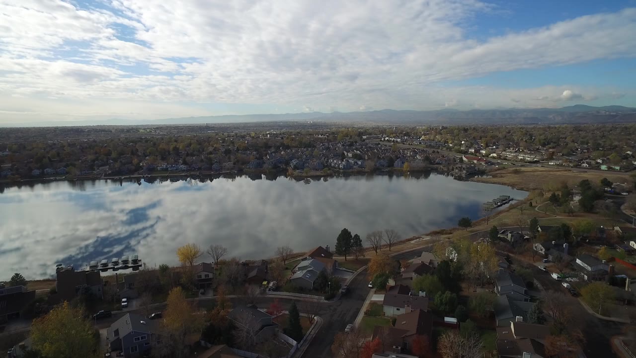 High aerial view of Hidden Lake, Colorado with foreground homes and roads, a reflective lake across the middle, distant neighborhoods and mountains, and no visible people.