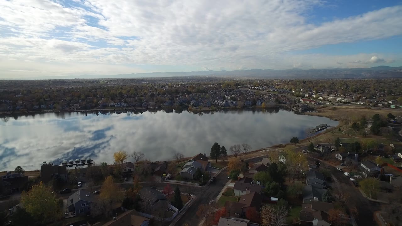 Aerial view of lakefront homes and roads with clouds reflected in the water.
