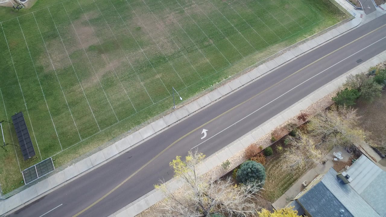 Overhead aerial view in Hidden Lake, Colorado showing a green lined field beside a diagonal two-lane road, sidewalk, trees, and no visible people.