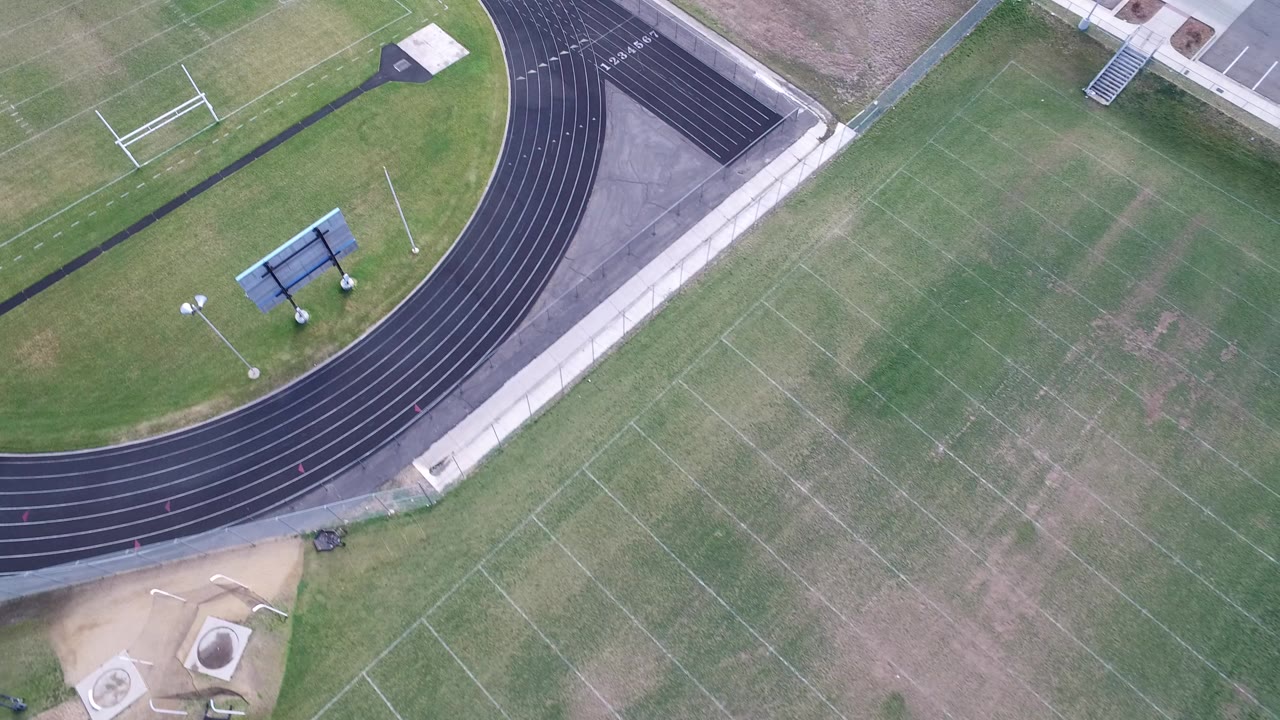 Overhead view of a green sports field and curved black running track.