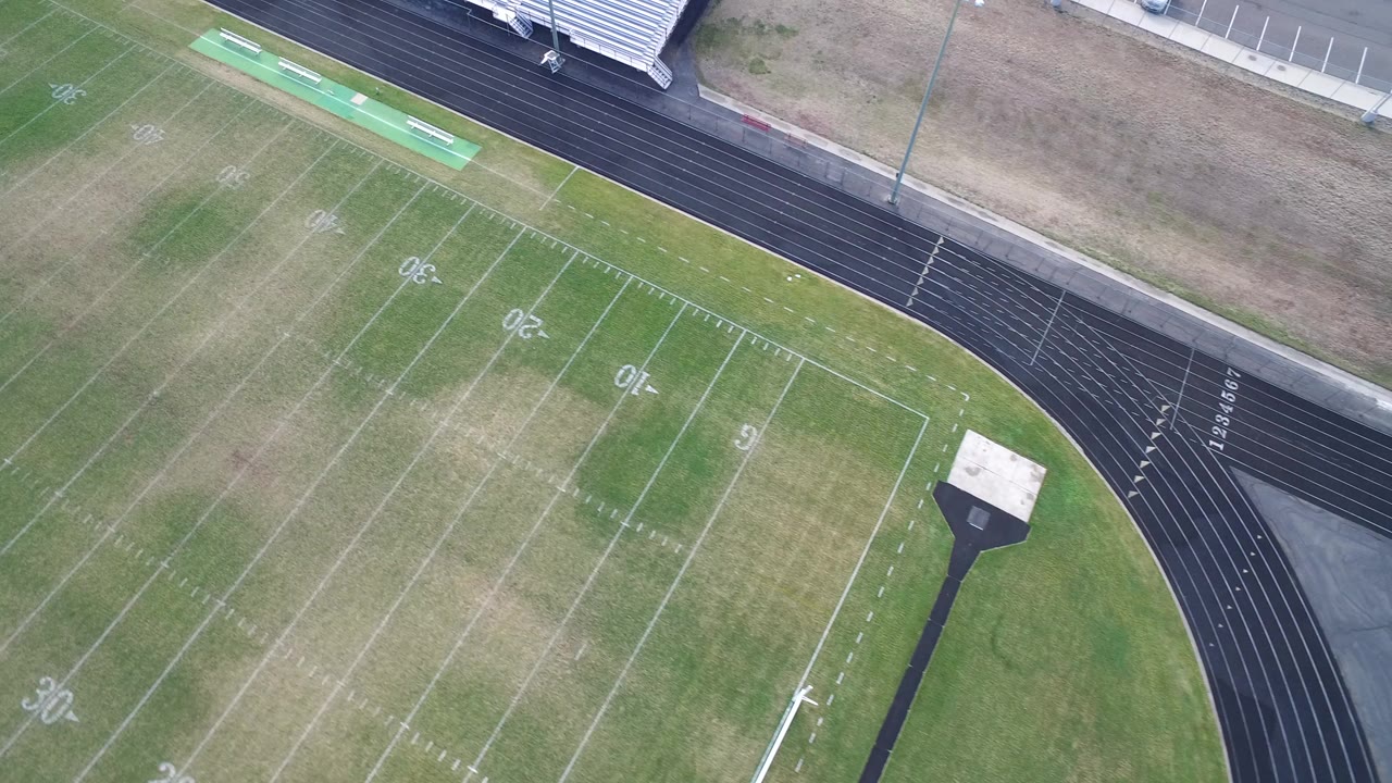 Aerial view in Hidden Lake, Colorado showing a marked football field with patchy green and brown grass, a black running track, metal bleachers, and no visible people.