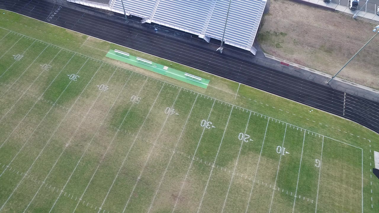 Overhead view of a green football field beside a black running track and metal bleachers.
