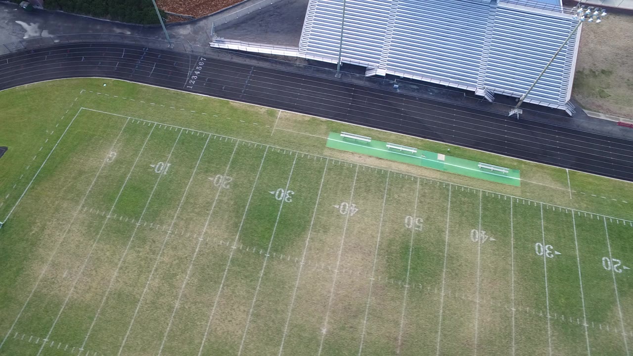 Overhead view of a football field beside a running track and bleachers.