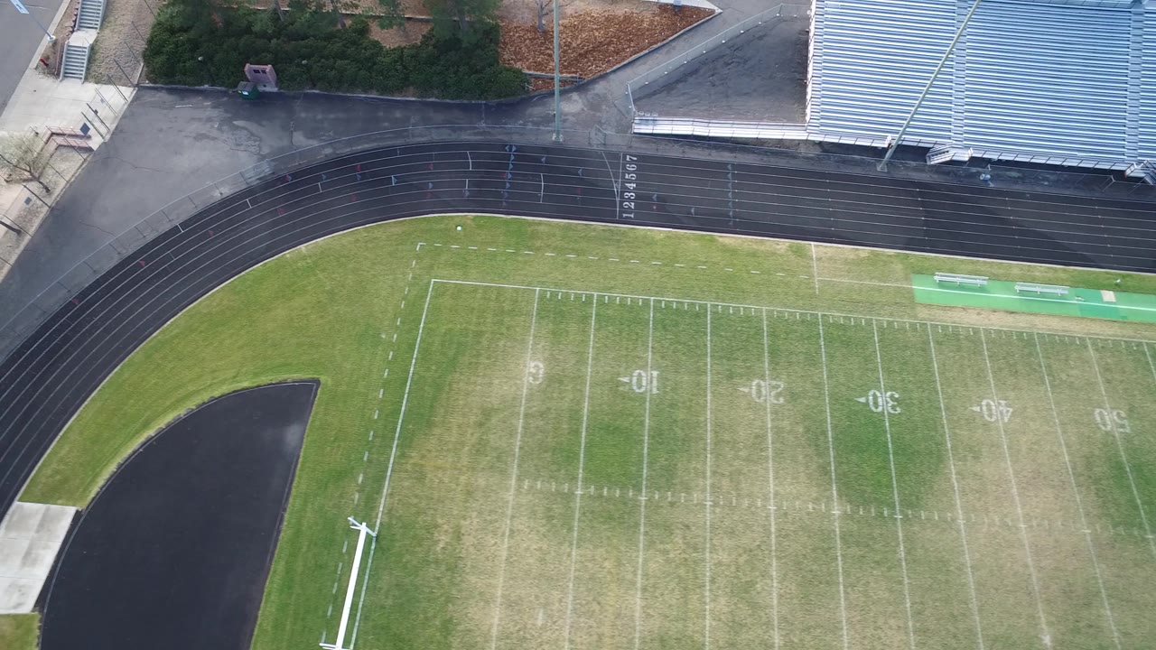 A high aerial frame over Hidden Lake, Colorado centers on the football field numbers and sideline markings, with the black track and metal bleachers along the upper edge and no visible people.
