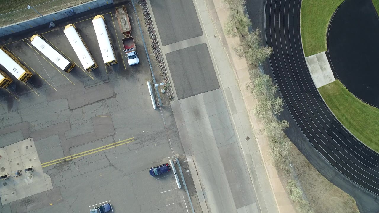 Overhead view of parked buses, cars, road, and running track.