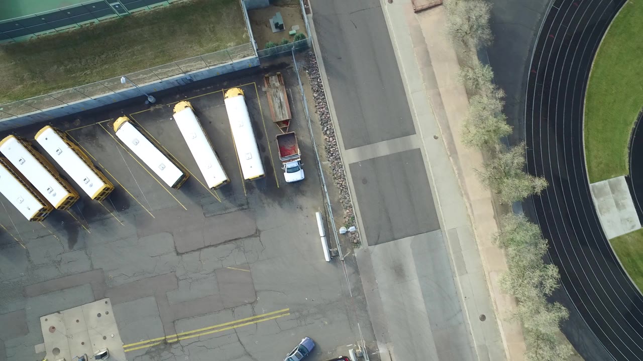 Top-down view of school buses parked beside a road and running track.