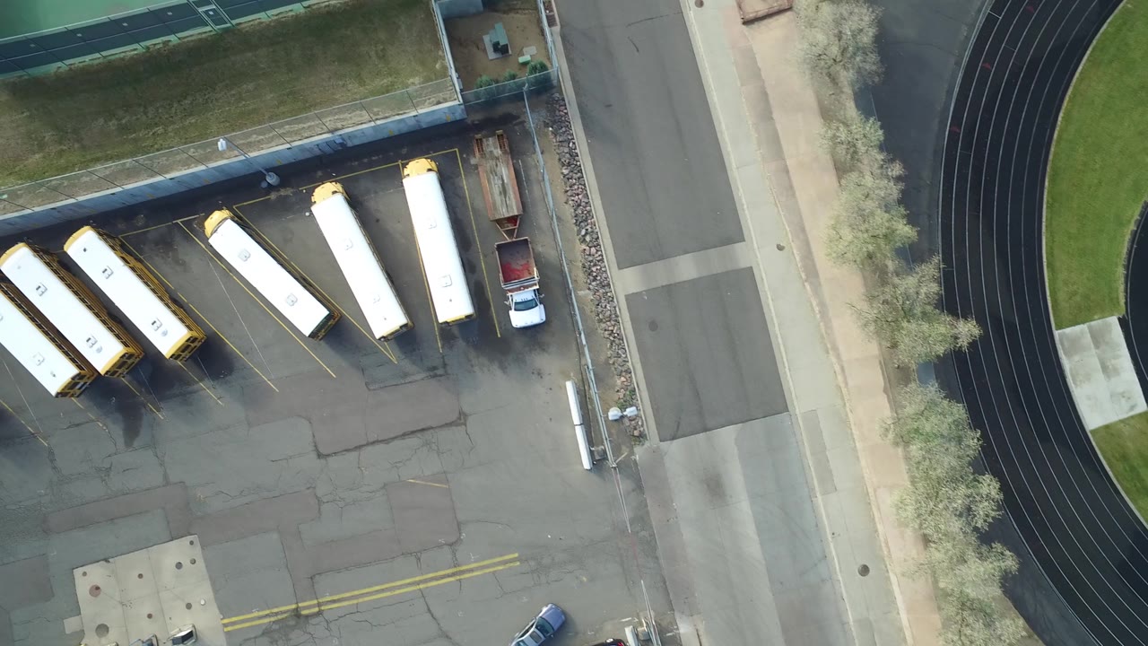 Second overhead frame in Hidden Lake, Colorado with the buses centered more clearly in marked parking spaces, the black track curving at right, roadside pavement, and no visible people.