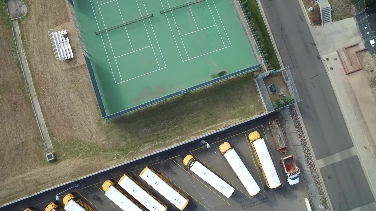 Overhead view of green tennis courts beside parked school buses and a street.