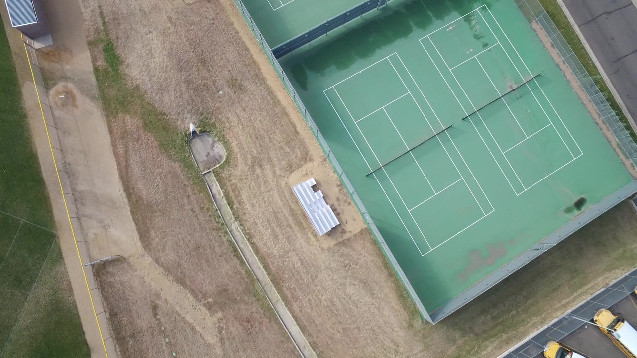 High overhead frame of a Hidden Lake, Colorado sports area with green tennis courts at upper right, dry ground through the center, grass at left, a path, and no visible people.