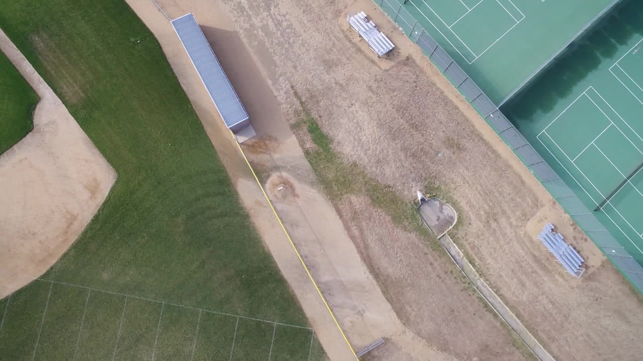 Aerial frame in Hidden Lake, Colorado, with the baseball infield edging into view, tennis courts at the upper right, bleachers near the courts, and no visible people.