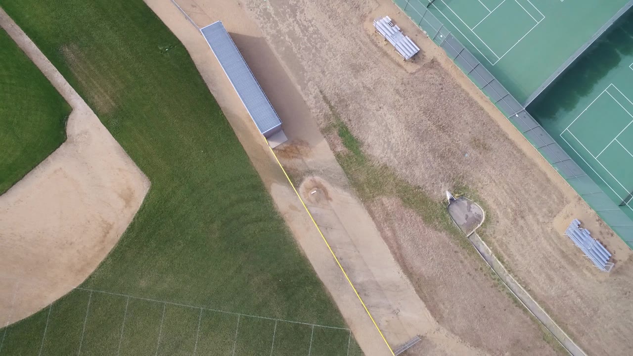 Aerial view of a baseball diamond, grass outfield, tennis courts, and sports facility paths.