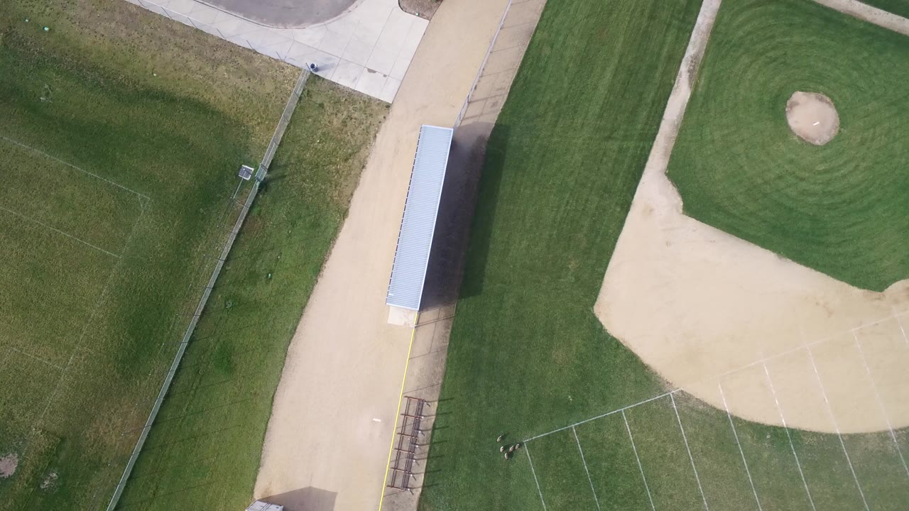 Overhead view of a green field beside a baseball infield and paved paths.
