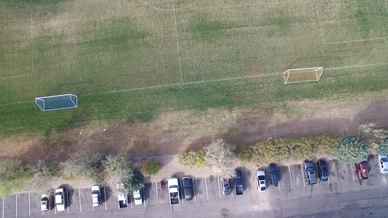 Overhead soccer field beside a parking lot with parked cars.