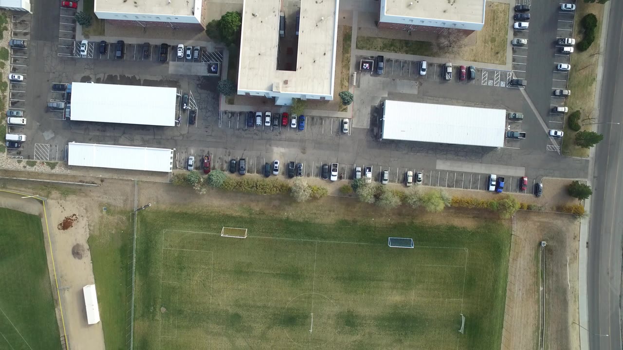 Overhead view of white commercial buildings, parking lots, road, and soccer field.