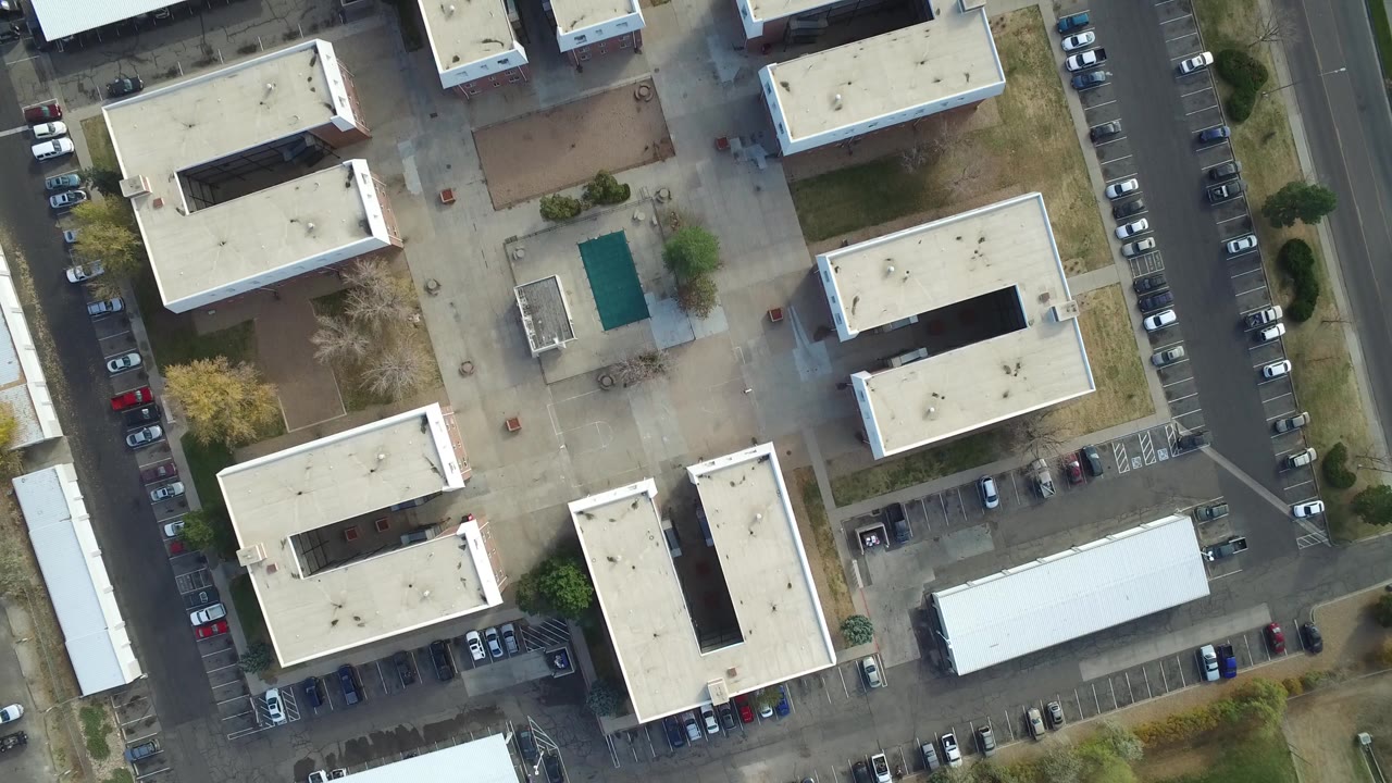 Top-down aerial view of white C-shaped buildings and parking rows.