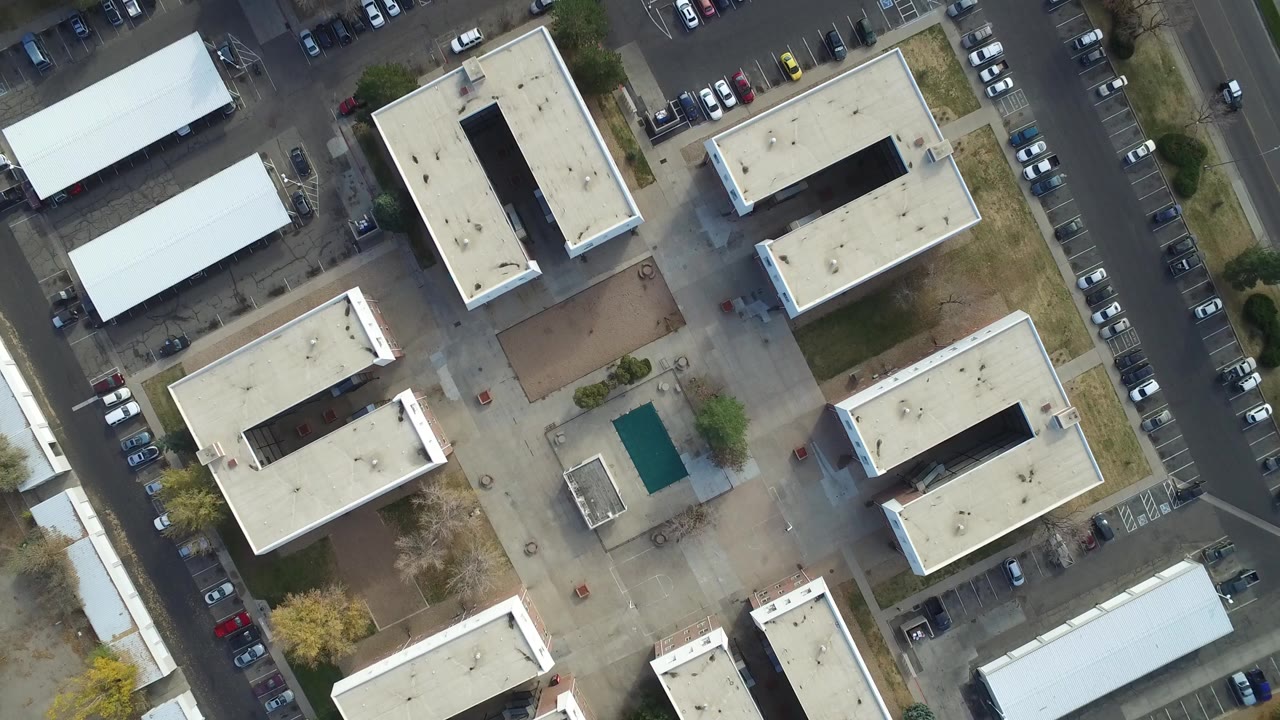 Overhead view of flat-roofed buildings, streets, and parking rows.