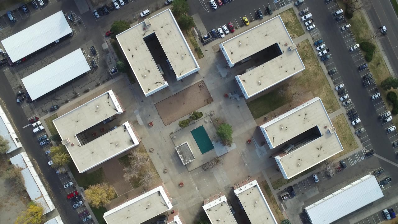 Second overhead frame in Hidden Lake, Colorado showing rectangular flat-roof buildings, a small green-roofed structure, parking lots, streets, and no visible people.