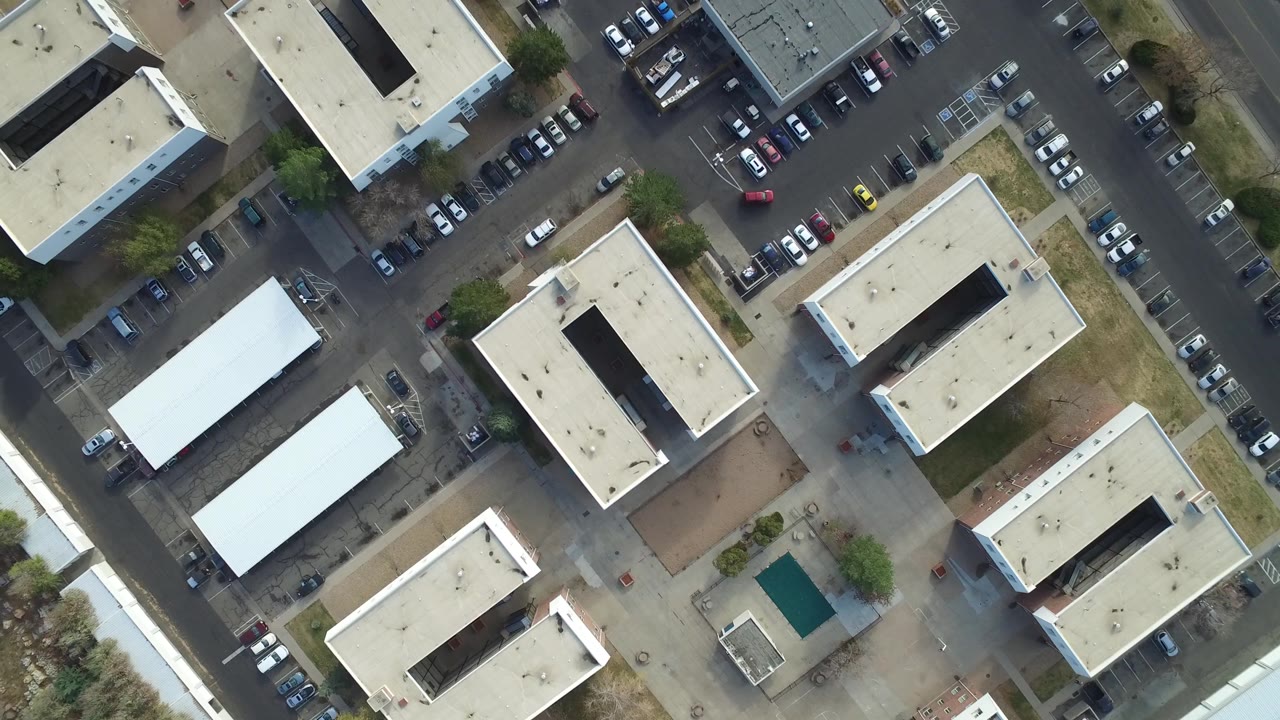 Aerial frame in Hidden Lake, Colorado with repeated rectangular office buildings, dark paved access roads, rows of cars, and no visible people.