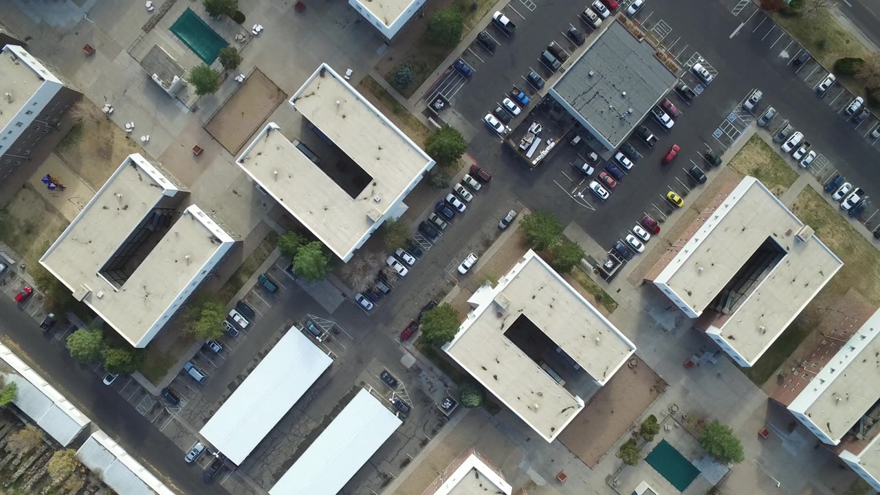 Hidden Lake, Colorado aerial frame with a dark-roofed building near the upper right, cream rooftops, parked vehicles, paved access lanes, and small figures by the pedestrian paths.