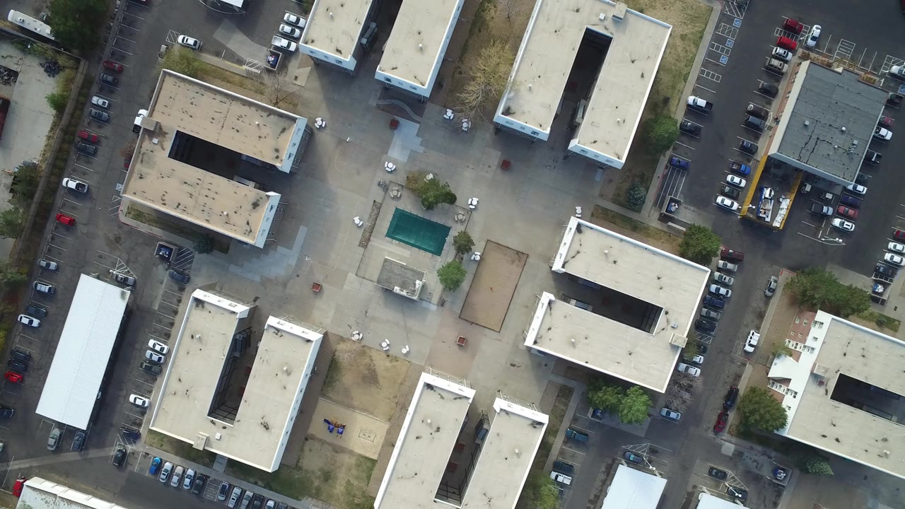 Straight-down aerial frame over Hidden Lake, Colorado showing flat beige rooftops, parked cars, paved lots, a small turquoise pool, and no visible people.