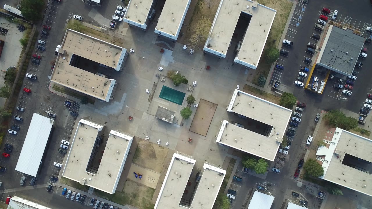 Aerial frame over Hidden Lake, Colorado with the turquoise pool nearer the center, low flat-roof buildings around it, parked cars along the streets, and no visible people.