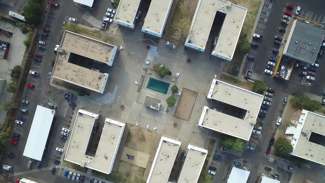 Vertical drone view of buildings, parking rows, and paved lots.