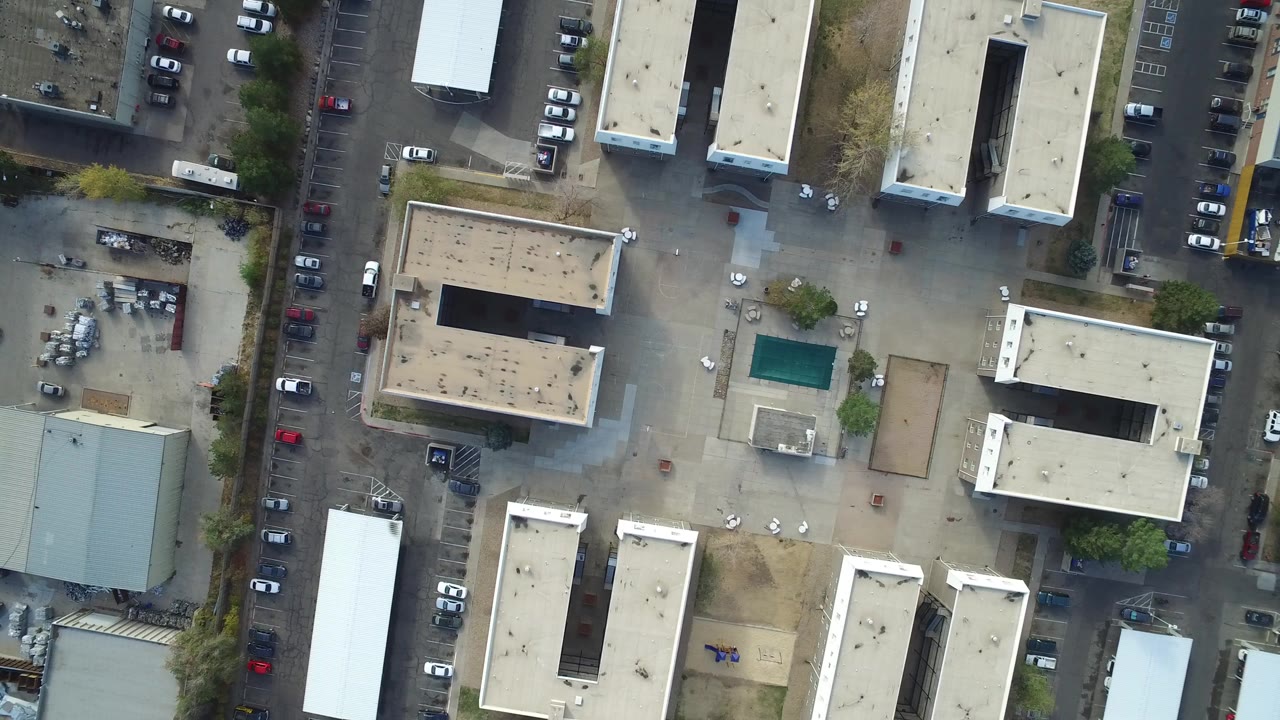 Vertical aerial frame over Hidden Lake, Colorado showing flat-roofed buildings, parking spaces, a street lined with cars, and no visible people.