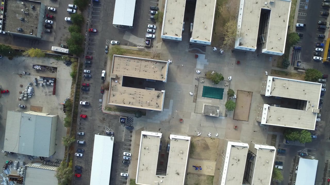 Aerial view of a street edge beside roofs and parking areas.