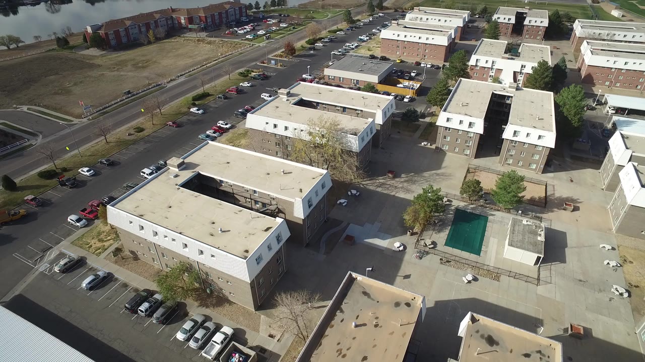 Aerial view of apartment buildings, parking lots, road, and water edge.