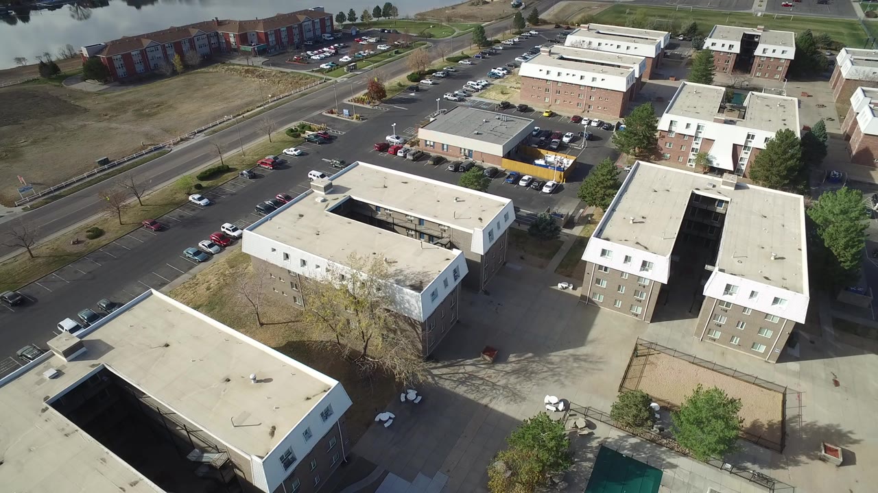 Aerial view over apartment buildings, parking lots, roads, and water in the background.