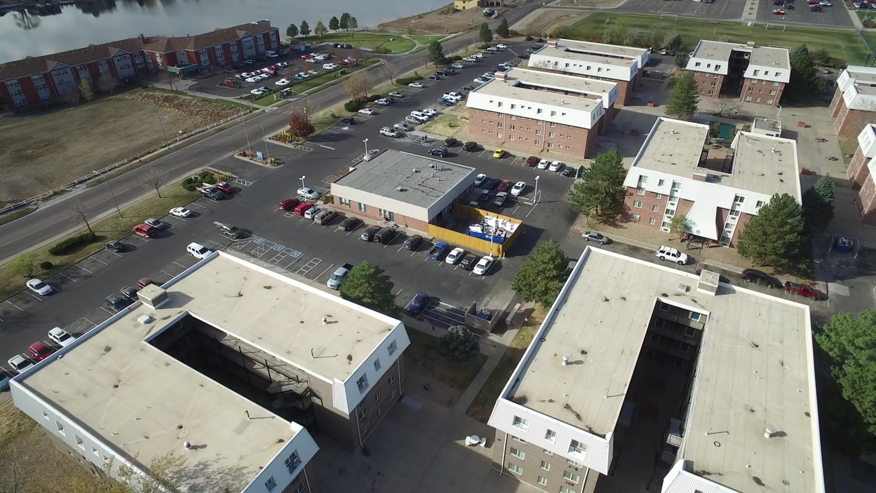 Aerial view of low-rise buildings, parking lots, roads, trees, and water beyond.